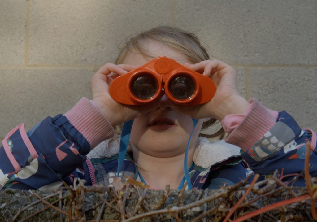 A young girl looks towards the camera using binoculars.